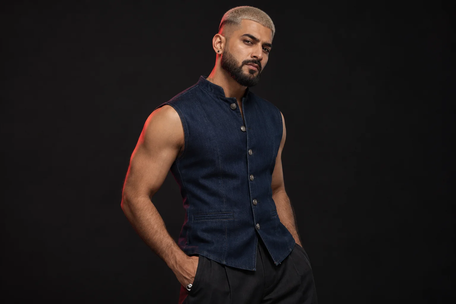 Man with a platinum buzz cut, precisely shaped black beard and navy sleeveless denim waistcoat