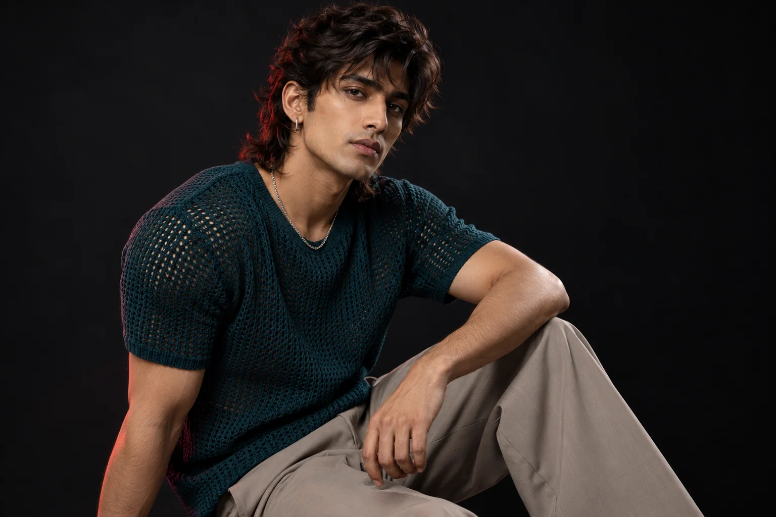 Man with a textured wolf cut and feathered nape, styled with a teal open-knit top and taupe trousers